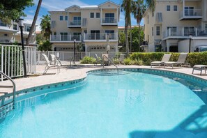 A swimming pool with lounge chairs and a fence, surrounded by multi-story buildings with balconies.