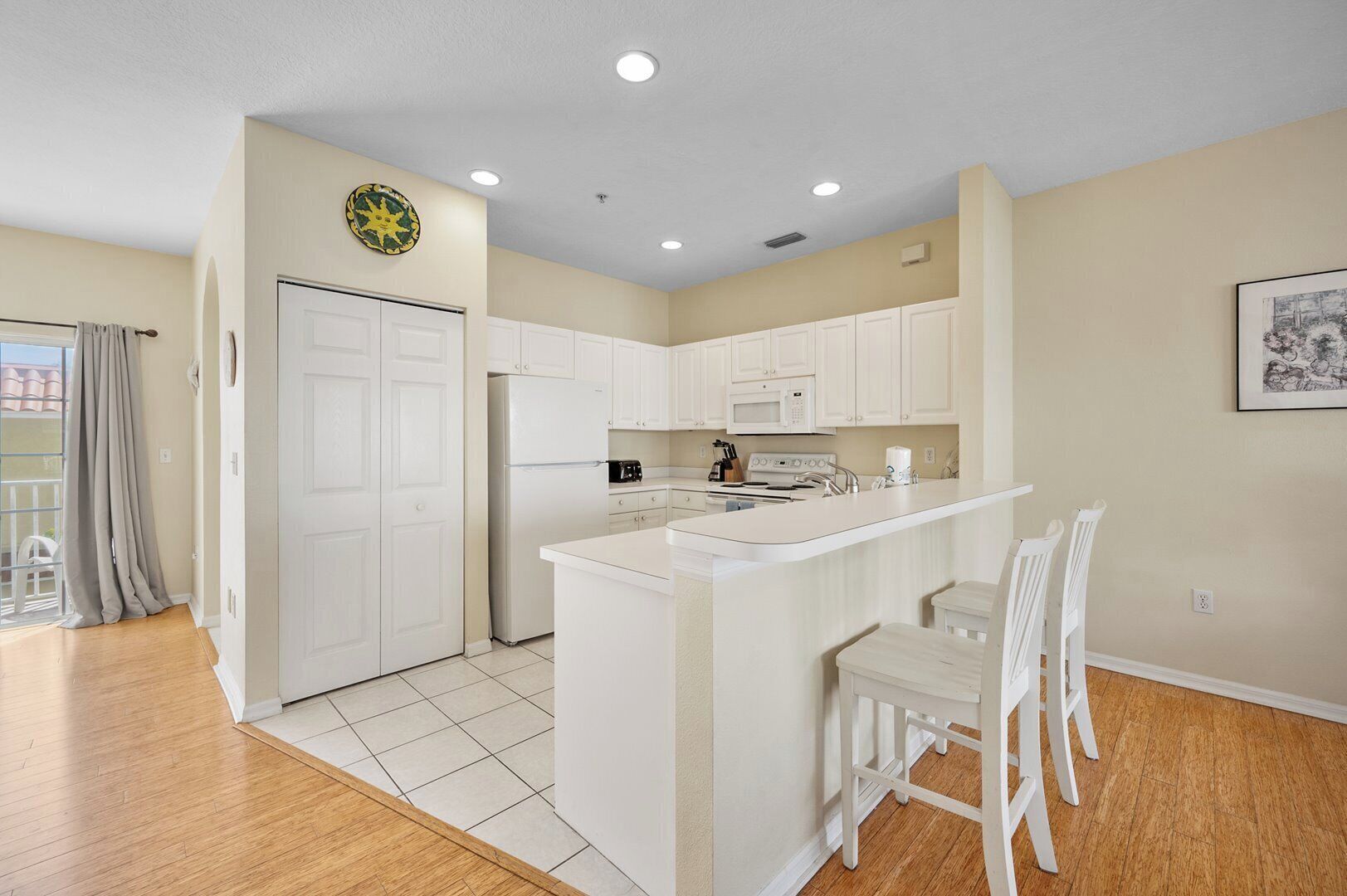 A modern kitchen with white cabinetry, a central island with bar stools, and a dining area.