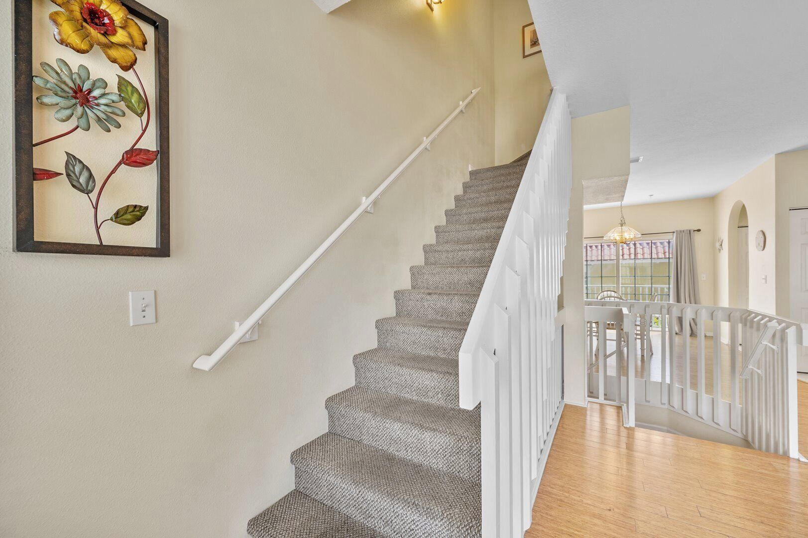 A staircase with a textured carpet, white handrail, and a framed floral artwork on the wall.