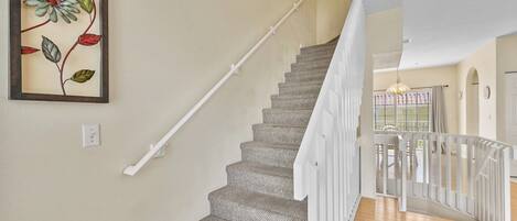 A staircase with a textured carpet, white handrail, and a framed floral artwork on the wall.
