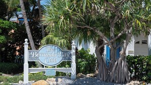 A sign for 'The Bermuda Bay Club' with a tropical backdrop including a large tree and a building with a blue door. - Wonderful townhouse located directly between the beach and the bay.  Watch the sunsets off the balco (BRADENTON BEACH)
