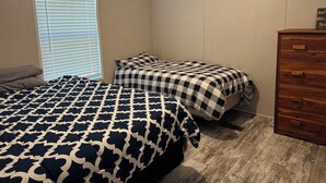 A bedroom with two beds, a dresser, and a window with blinds.
