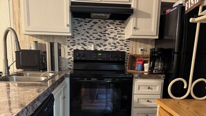 A kitchen with white cabinets, a black oven, a microwave, a coffee maker, and a wooden table.
