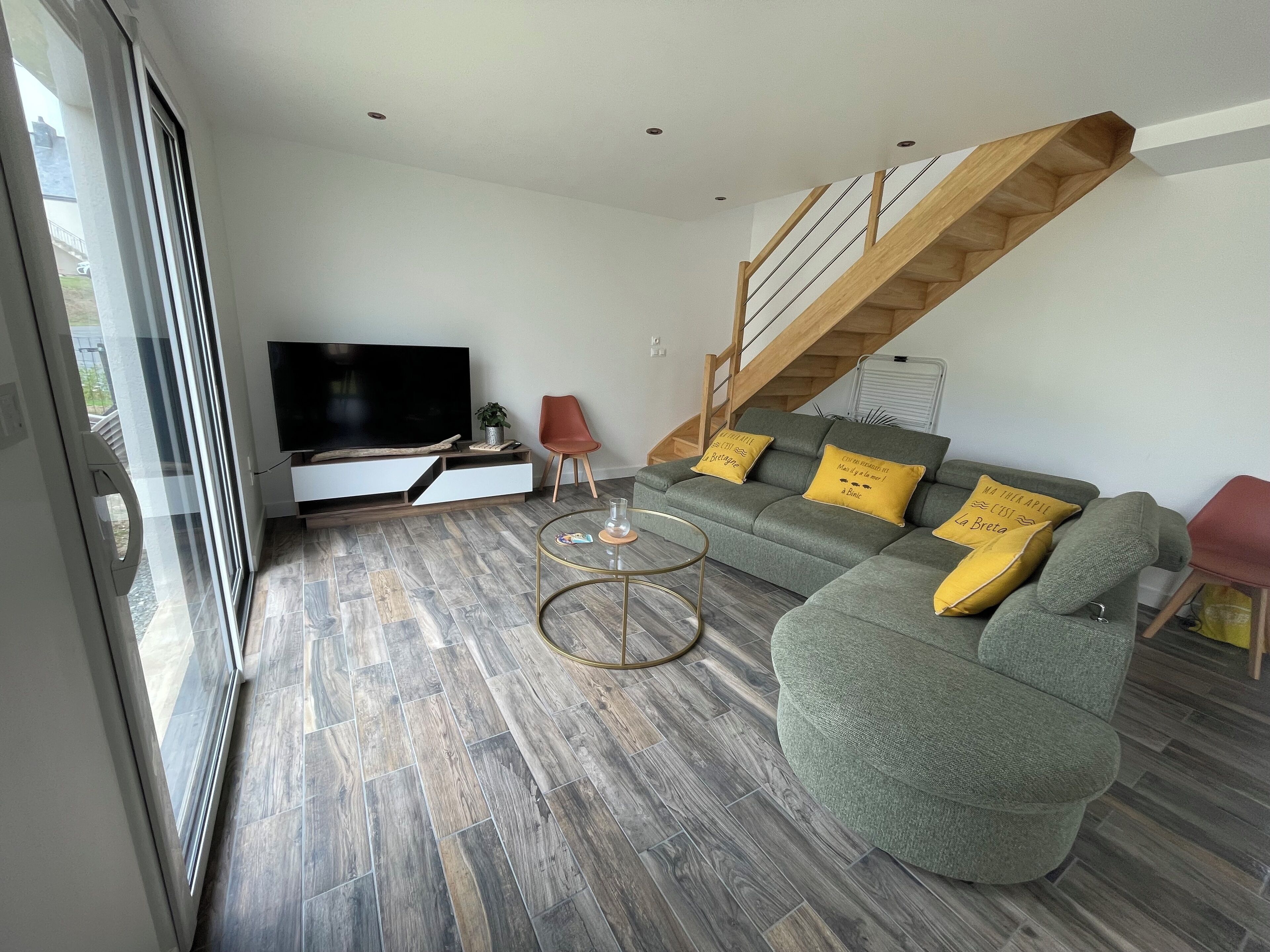 Una sala de estar moderna con un sofá seccional gris, un televisor de pantalla plana y una escalera de madera.