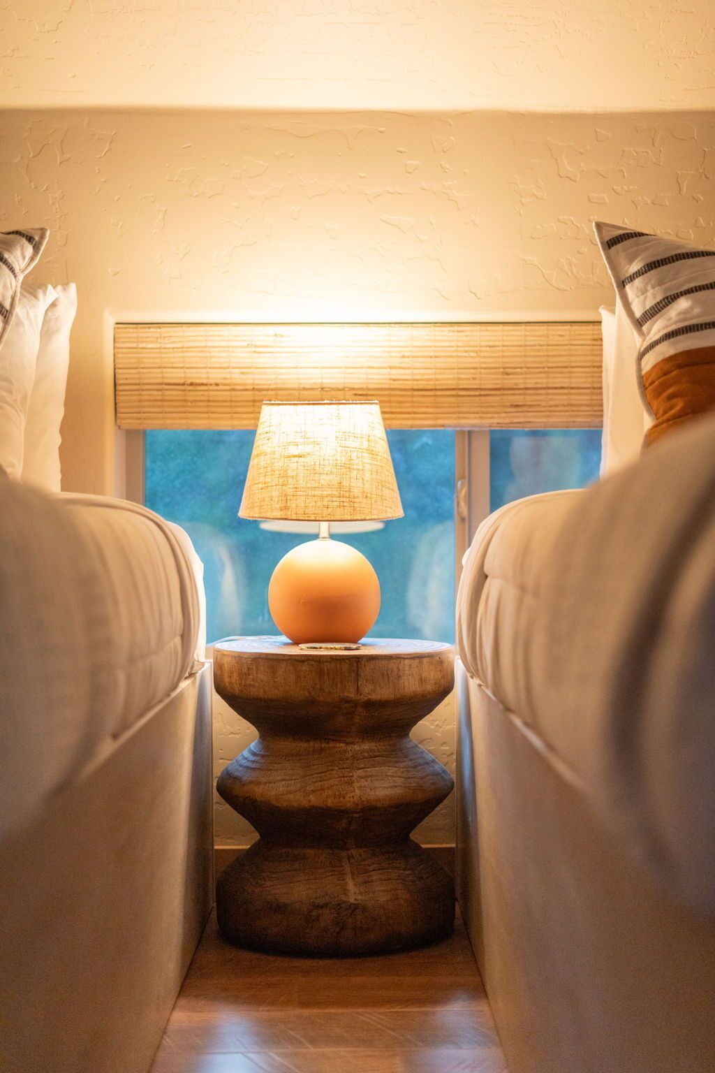 A cozy room with a lamp on a wooden stand, a window with a view, and a couch.