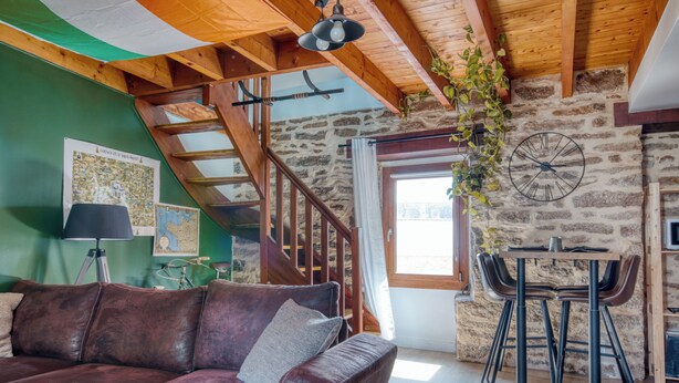 Un interior rústico con una escalera de madera, un sofá de cuero, una mesa de comedor con sillas y una pared de piedra.