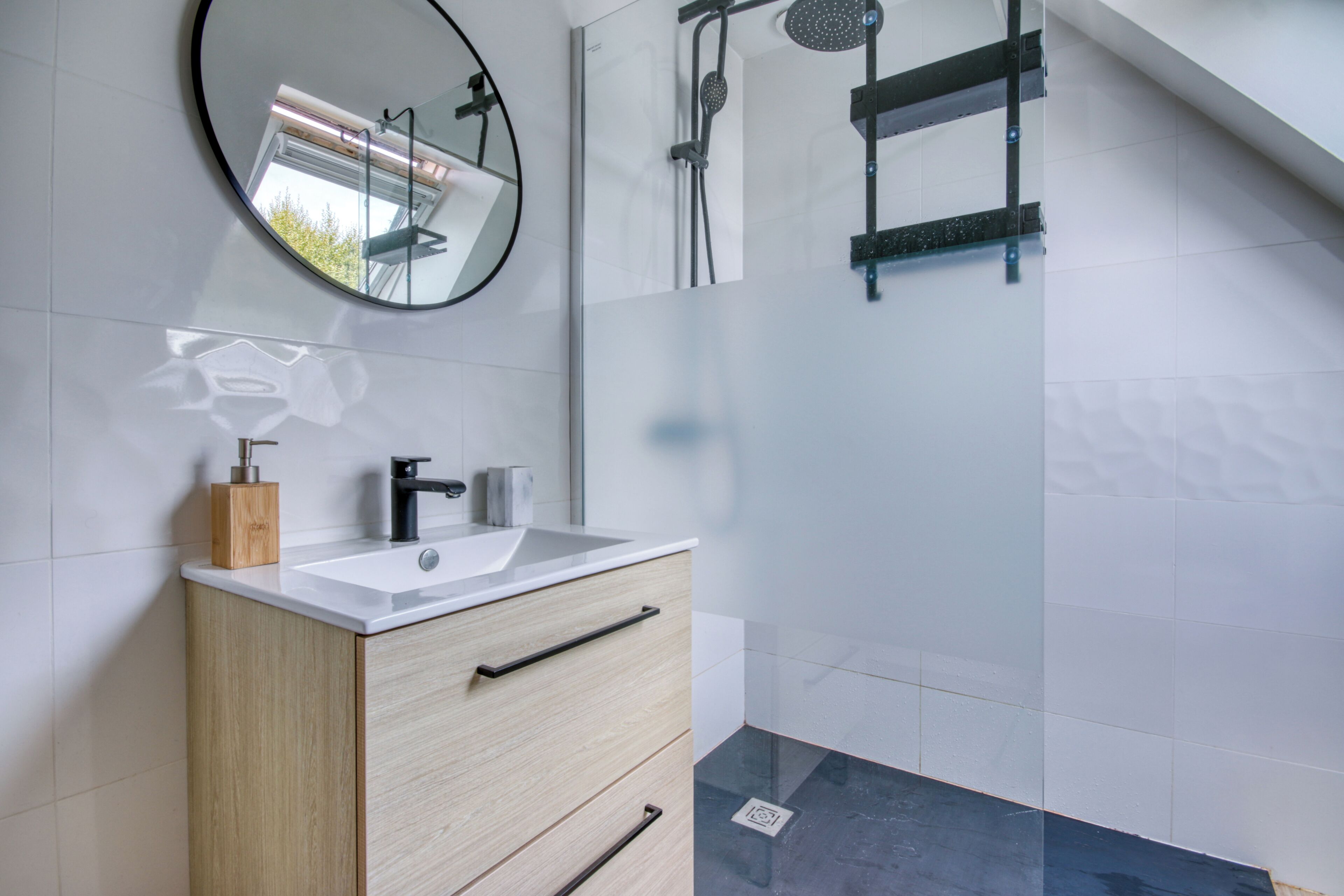 A modern bathroom with a white sink, wooden cabinet, and a round mirror.