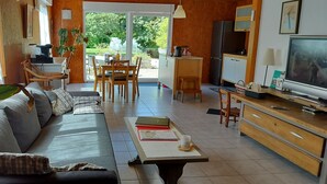 Una sala de estar moderna con un sofá, una mesa de centro y un televisor. Hay un comedor con una mesa y sillas, y un área de cocina con un refrigerador y un microondas.