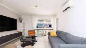 En moderne stue med en grå sofa, et fladskærms-tv, et rundt sofabord og en balkon med stribede markiser.