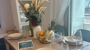 Et spisebord dækket med tallerkener, bestik, en vase med tørrede blomster, en frugtskål og en vinflaske.