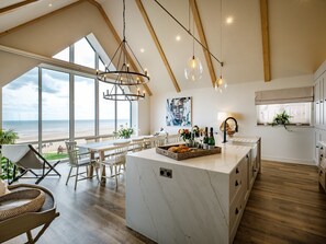 Une cuisine spacieuse dotée d’un grand îlot central, de poutres en bois et de grandes fenêtres donnant sur la plage.