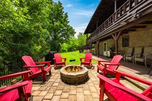A patio with red Adirondack chairs, a stone fire pit, and a grassy lawn. - Peaceful Path-Smoky Mountains, TN with Hot Tub (Sevierville)