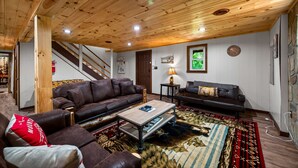 A wooden ceiling, a brown leather sofa, a coffee table, and a patterned rug in a room with a staircase. - Secluded 4BR Cabin | Hot Tub, Pool Table, Arcade (Sevierville)