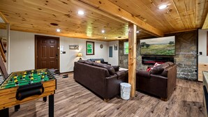 A cozy living room with a foosball table, a stone fireplace, and a comfortable sofa. - Secluded 4BR Cabin | Hot Tub, Pool Table, Arcade (Sevierville)