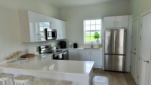 Una cocina moderna con muebles blancos, electrodomésticos de acero inoxidable, una isla grande con taburetes y una ventana con vistas a zonas verdes.