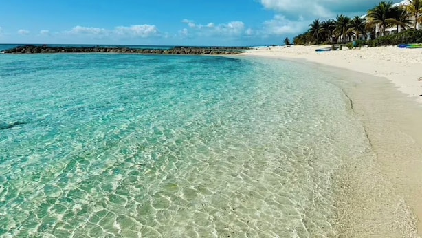 Una playa con agua turquesa cristalina, arena blanca y una barrera rocosa.
