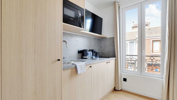 A modern kitchen with a microwave, coffee maker, and a window with curtains. - Cosy Apartment - 2P - Montreuil (Montreuil)