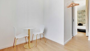 A room with a round table and two chairs, a coat rack, and a bed in the background. - Cosy Apartment - 2P - Montreuil (Montreuil)