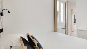 A bedroom with a bed, a wall-mounted lamp, and a window with curtains. - Cosy Apartment - 2P - Montreuil (Montreuil)