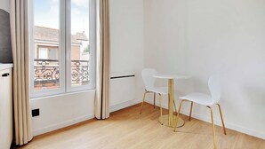 A room with a window, a radiator, a white table with two chairs, and a wooden floor. - Cosy Apartment - 2P - Montreuil (Montreuil)