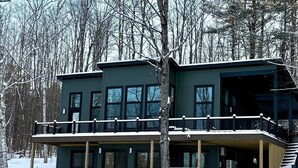 Een tweelaags vakantiehuis met een balkon en een overdekte veranda, omringd door sneeuw en bomen.