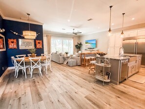 A modern kitchen with stainless steel appliances, a dining area with white chairs, and a living room with a sofa and a TV. - Luxury beach escape, 2 blocks to the ocean & 1 block to the river! Sauna, heated pool, hot tub, paddle boards, kayaks, golf cart & more—only 10 mins to downtown St. Augustine. Very clean, well stocked & perfect for couples, families & small groups. (St. Augustine)