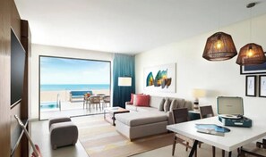 A modern hotel room with a large window, a sofa, a dining table, and a laptop.