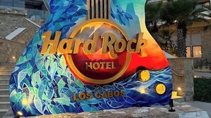 A Hard Rock Hotel sign with a guitar design, located in front of a building with multiple balconies.
