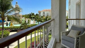 Un balcón con vistas a una piscina, palmeras y un edificio con una torre de reloj.