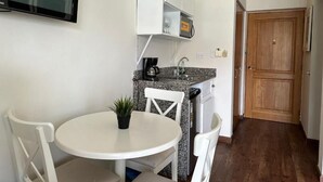 A compact kitchen with a white table and chairs, a small countertop with a coffee maker, and a wooden door in the background. - Hotel Palmera Bayahibe - One-Bedroom Villa 2 (República Dominicana)