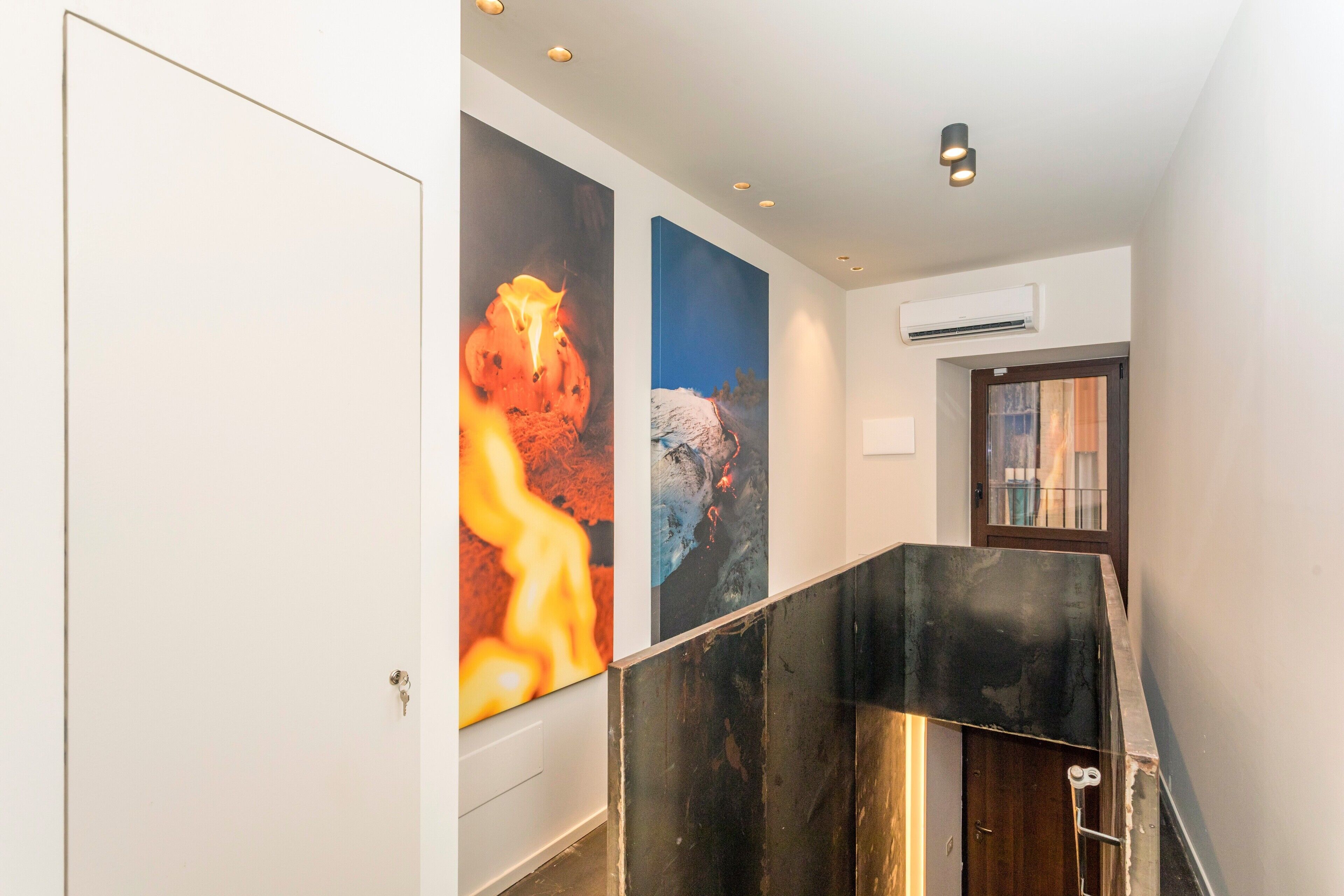 A hallway with a staircase, a door, and two large wall-mounted artworks.