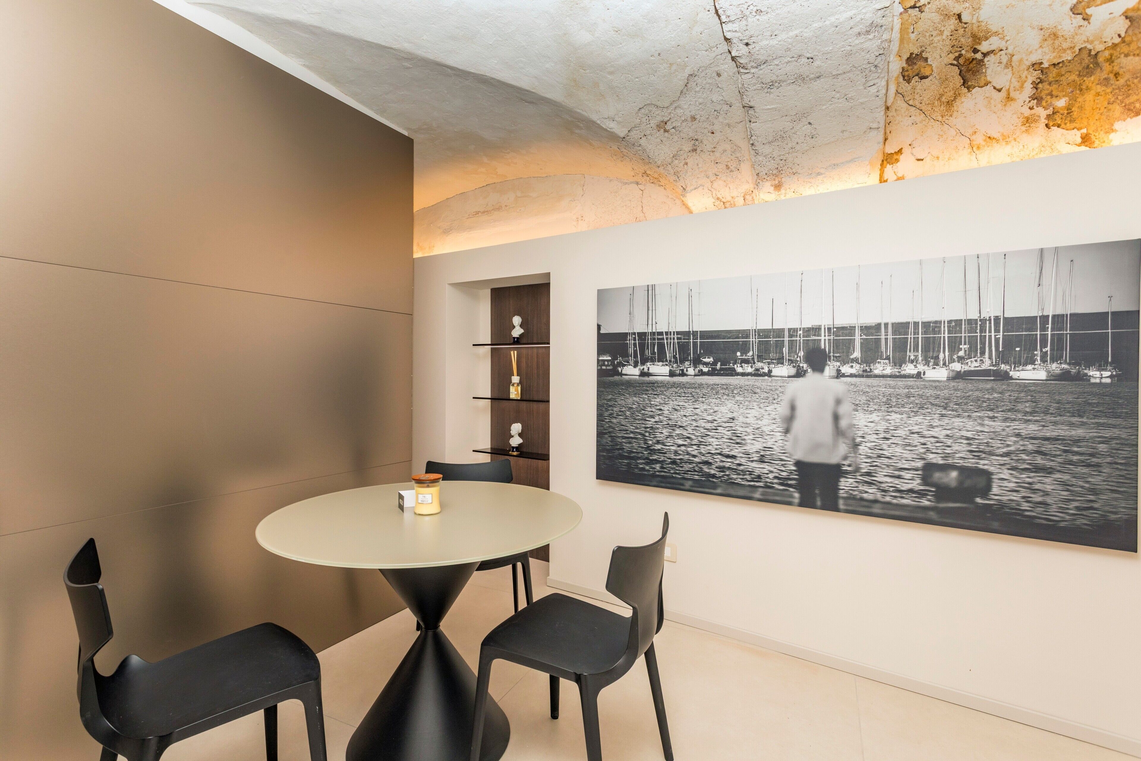 Un comedor moderno con una mesa redonda y sillas, una fotografía grande en blanco y negro de barcos en el agua y un techo con textura.
