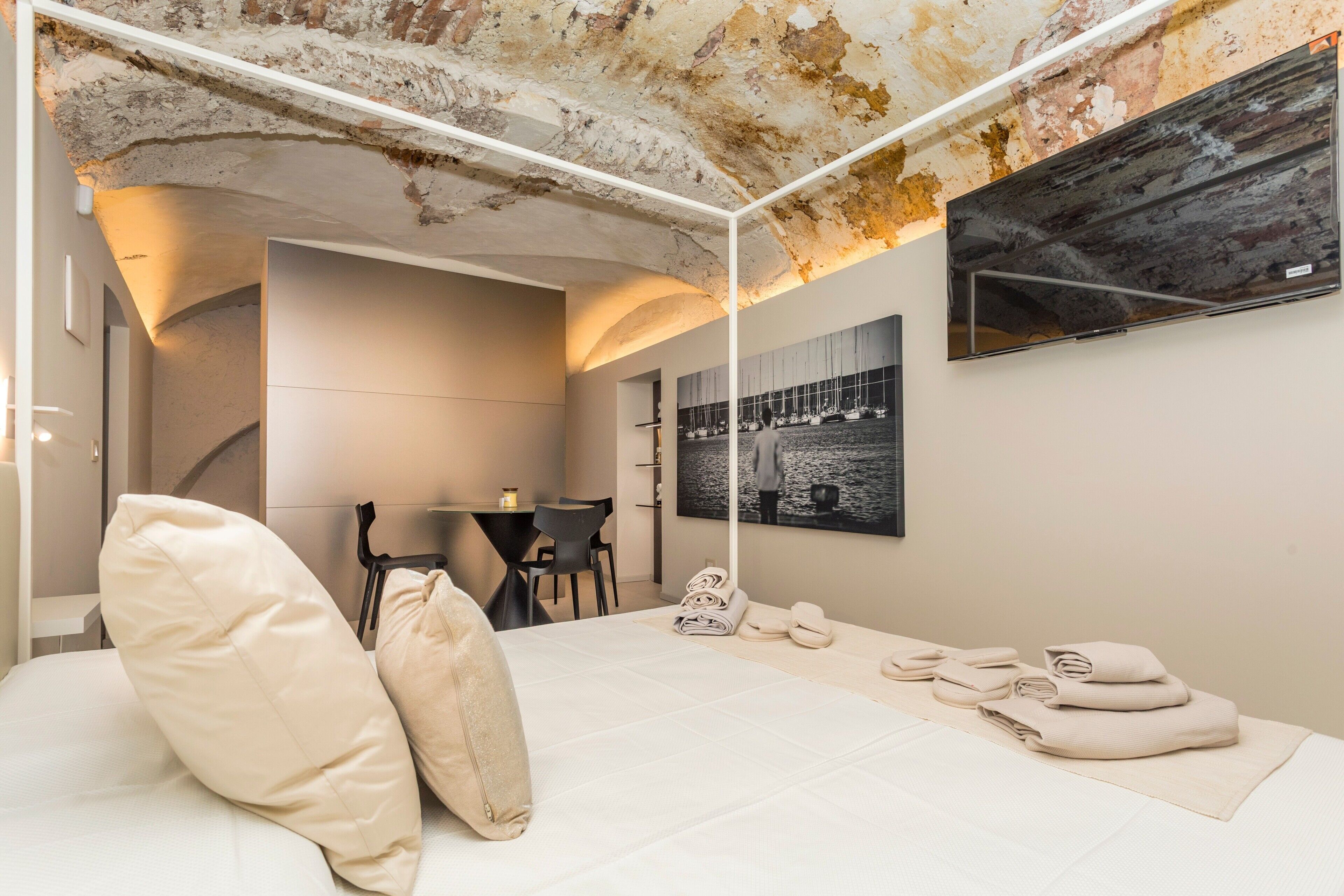 Une chambre à coucher avec un lit, des oreillers, un bureau, des chaises, une télévision et des œuvres d’art accrochées au mur.