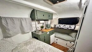 A compact RV interior with a bunk bed, kitchenette, and a patterned bedspread.