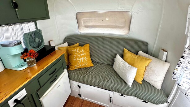 A compact RV interior with a kitchenette, a bed with striped bedding, and a small window.