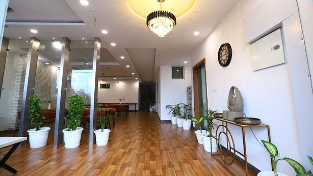 A spacious lobby with wooden flooring, a chandelier, potted plants, and a clock on the wall. - Hotel The Anvi Residency Sector 132 (Noida)