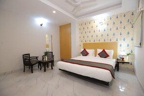 A hotel room with a large bed, a desk, two chairs, a small table, and a nightstand with a lamp. - Hotel The Anvi Residency Sector 132 (Noida)