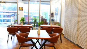 A modern cafe with wooden tables and orange chairs, large windows, and a brick wall. - Hotel The Anvi Residency Sector 132 (Noida)