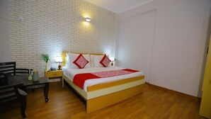 A bedroom with a wooden floor, a bed with white and red bedding, a nightstand with a lamp, and a brick-patterned wall. - Hotel The Anvi Residency Sector 132 (Noida)