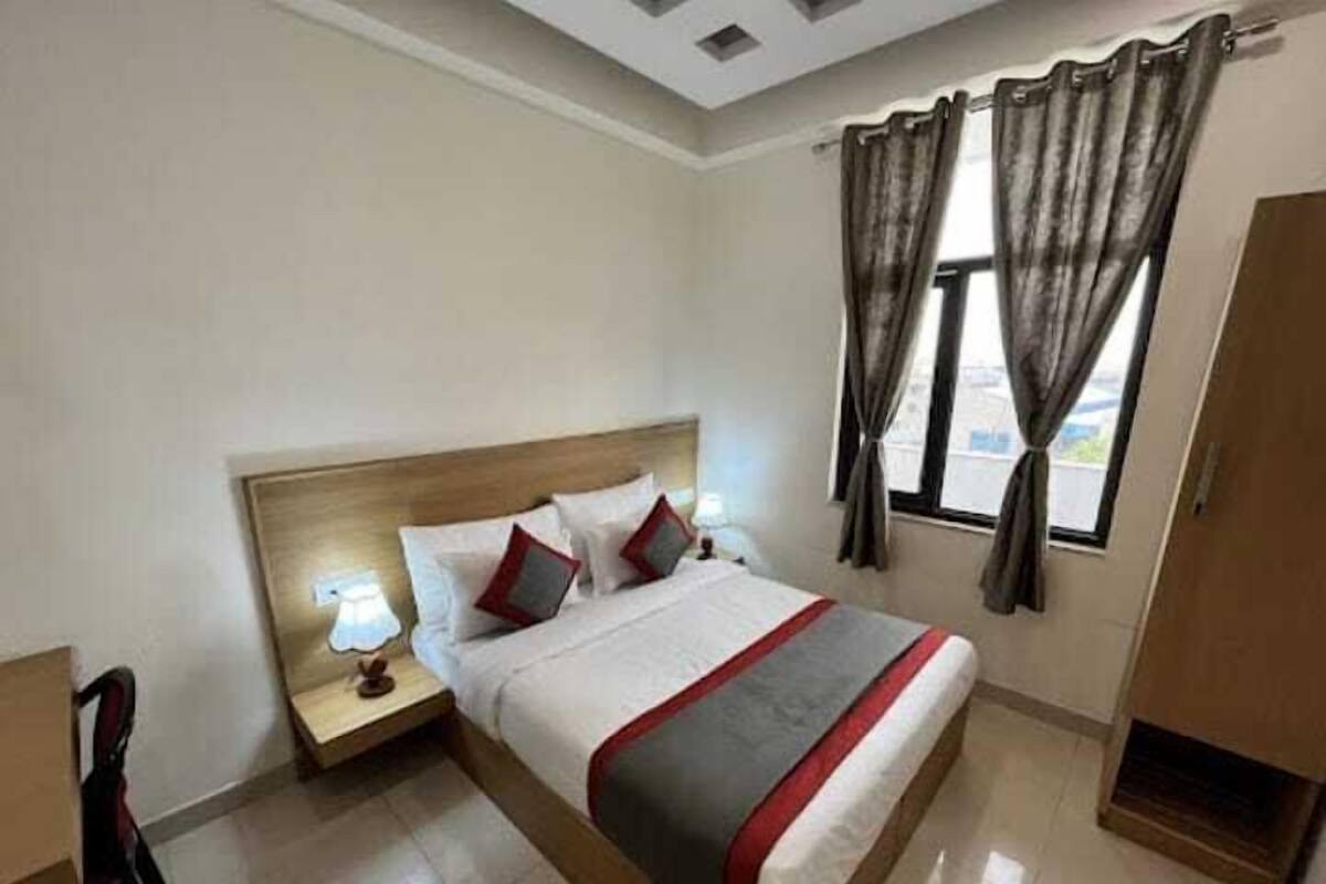 A hotel room with a bed, bedside tables, a chair, a wardrobe, and a window with curtains.