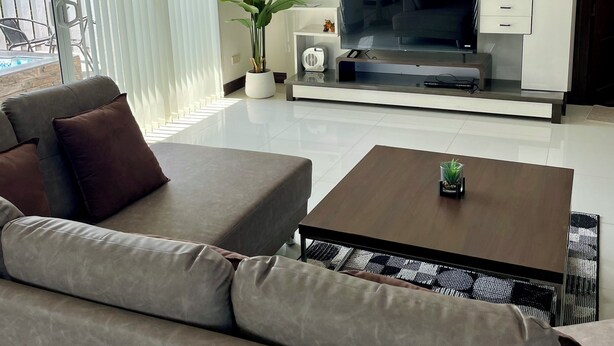 Un salon moderne avec un canapé gris, une table basse, un téléviseur à écran plat et un meuble blanc avec des tiroirs.