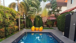 Une piscine rectangulaire avec une terrasse carrelée, entourée de plantes tropicales et d’un palmier.