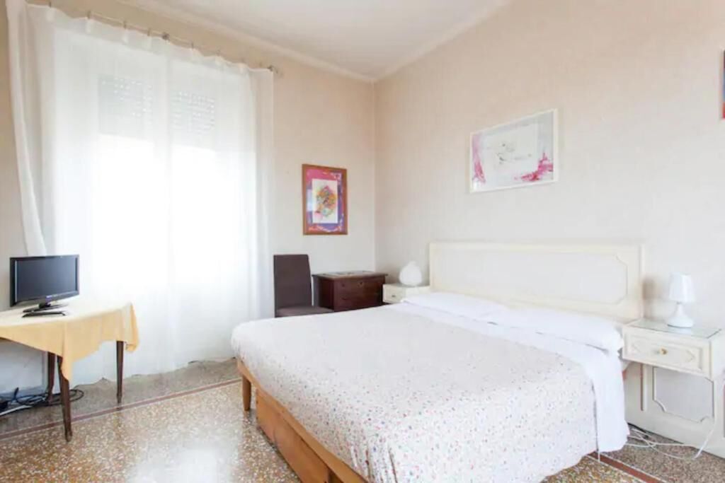 A bedroom with a bed, a desk, a chair, a nightstand, and a wall with two framed pictures.