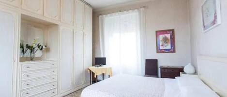 Un dormitorio con cama, escritorio, silla, armario y ventana con cortinas.