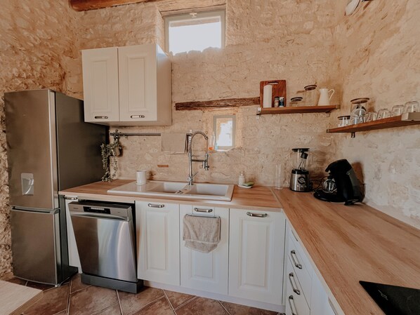 A compact kitchen with white cabinets, a stainless steel refrigerator, a dishwasher, and a coffee maker. - La Maison des Pierres Blondes, a vacation home in the countryside! (Orban)