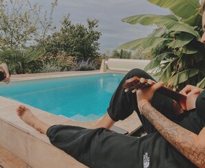A person relaxing by a pool with a toy car, surrounded by greenery and a clear sky. - La Maison des Pierres Blondes, a vacation home in the countryside! (Orban)