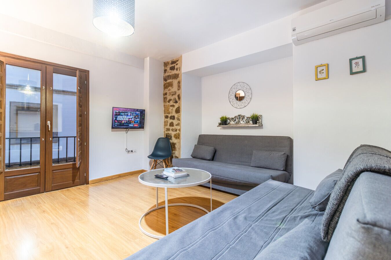 Een moderne woonkamer met een grijze bank, een ronde salontafel en een aan de muur bevestigde televisie.