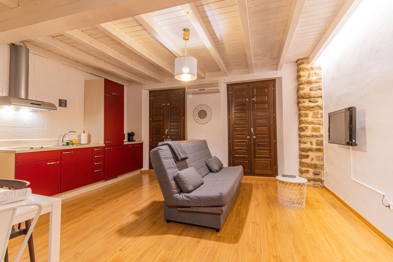 Un espacio habitable compacto con kitchenette, un sofá gris y una pared de piedra.