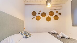 Un lit bien fait, agrémenté d’un coussin décoratif, un mur orné de motifs circulaires tissés et une serviette enroulée posée sur une table de chevet.