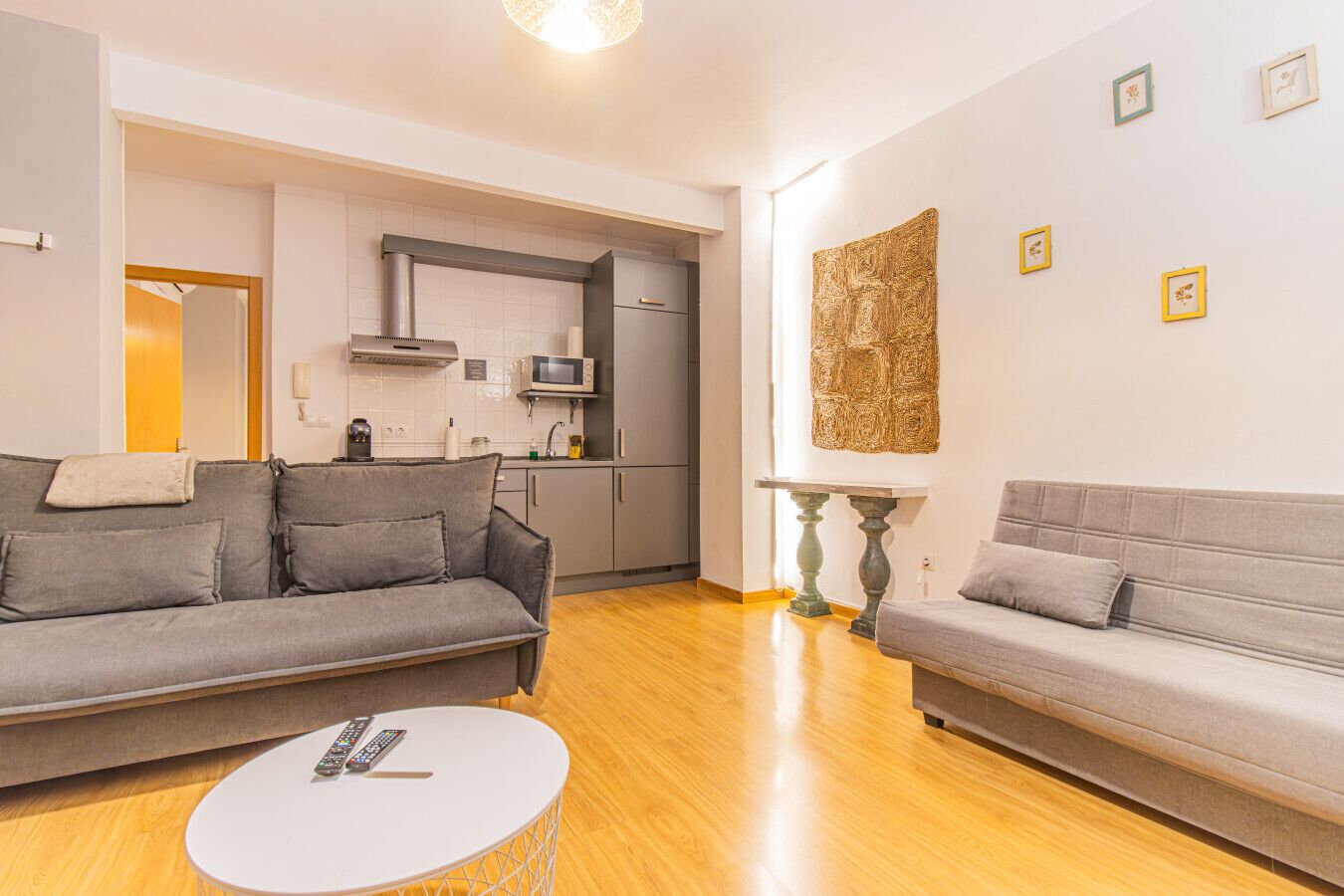 Een moderne woonkamer met twee grijze banken, een klein witte salontafel en een keuken op de achtergrond.